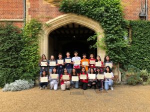 A group of Reach Cambridge students proudly display their certificates while posing in front of a historic Cambridge University building.