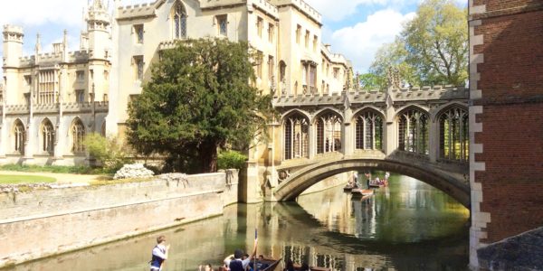 Students punting on the River Cam under the historic Bridge of Sighs at St John's College, Cambridge, on a sunny day.